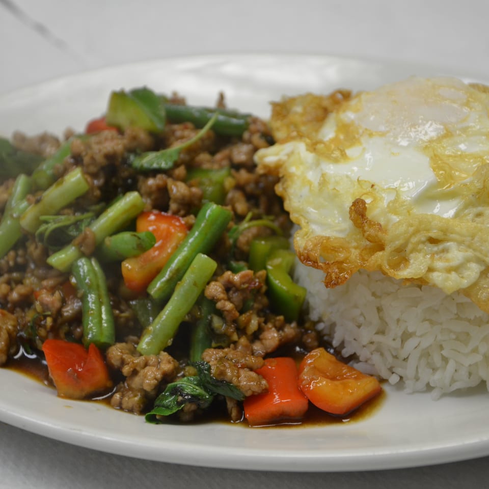 Thai-style minced pork stir-fried with green beans and vegetables, served beside steamed rice topped with a crispy fried egg.
