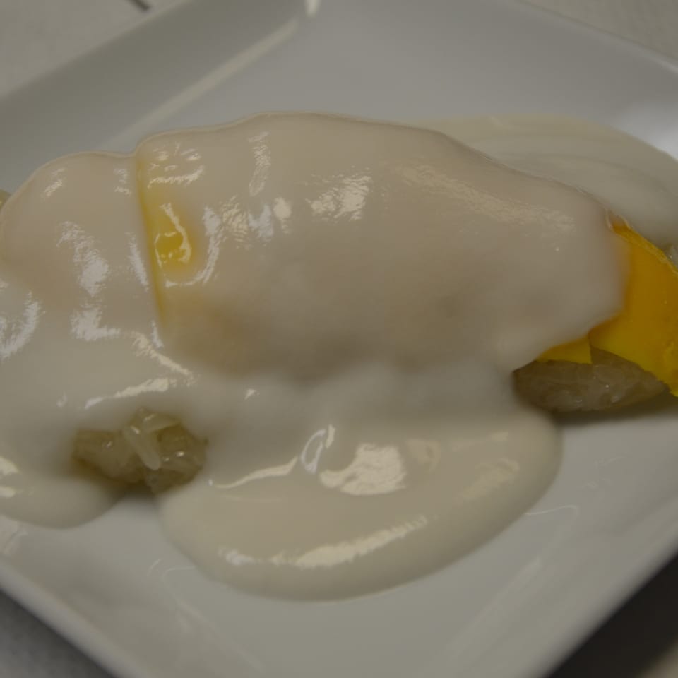 Poached egg with runny yolk served over creamy white sauce and garnished with yellow vegetables on a white plate.