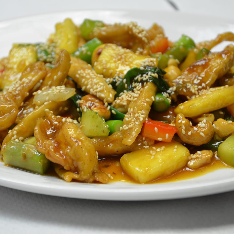 Glazed stir-fried chicken with mixed vegetables, cashews, and sesame seeds served on a white plate.