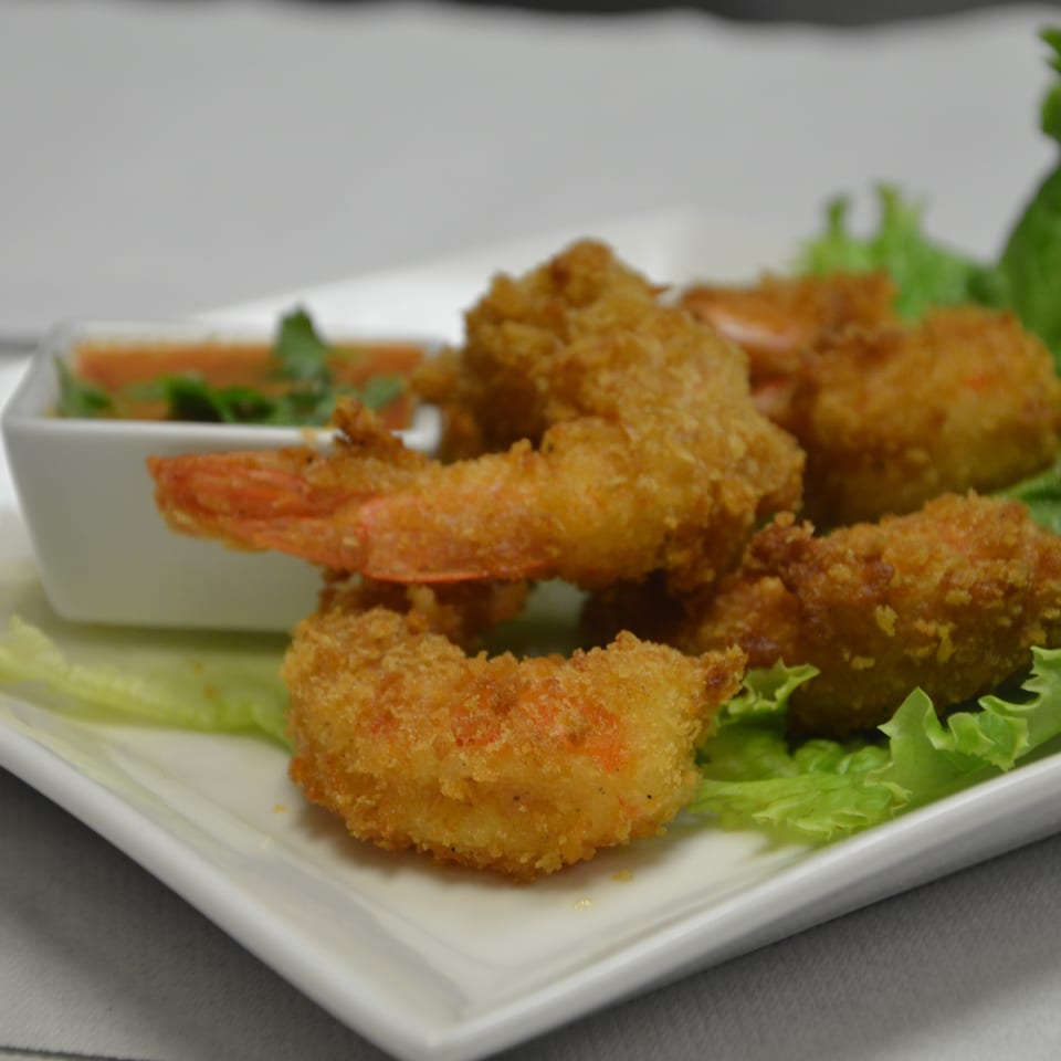 Crispy breaded shrimp served on lettuce with a small dish of dipping sauce.