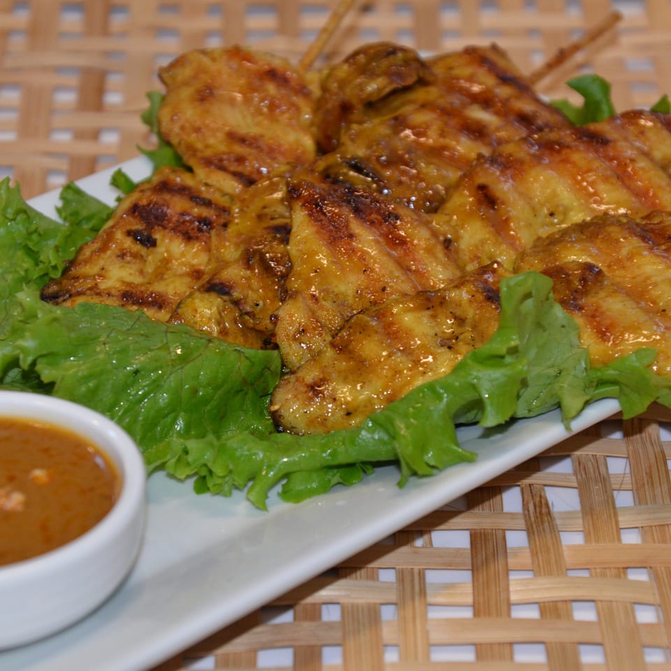 Grilled golden chicken skewers served on lettuce with carrots and dipping sauce on a white platter.