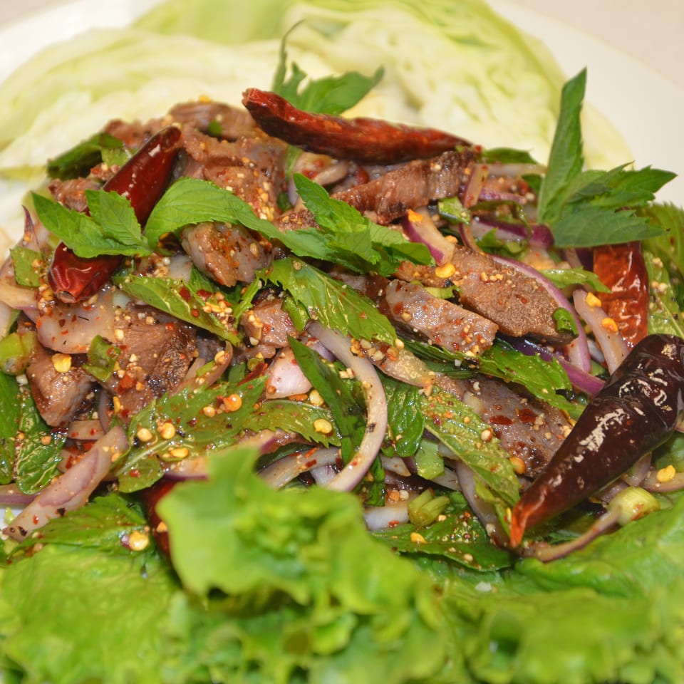 Spicy grilled beef salad with herbs, red onion, dried chilies, and lettuce garnish on a white plate.