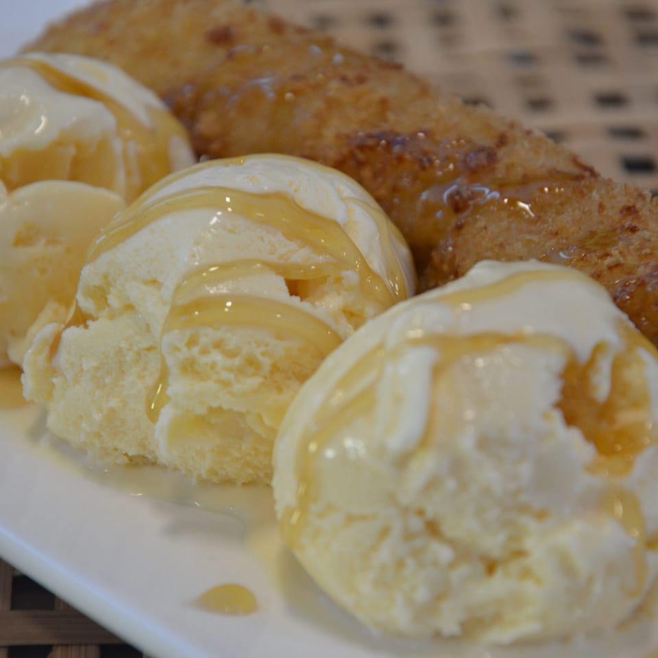 Scoops of vanilla ice cream drizzled with caramel beside golden breaded pastries on a white plate.