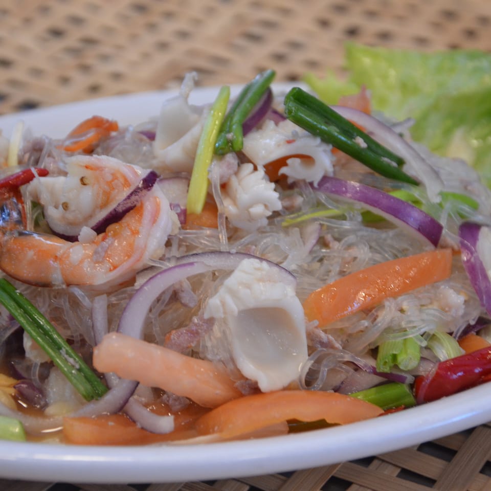 Thai-style glass noodle salad with shrimp, squid, onions, tomatoes, scallions, chilies, and lettuce.