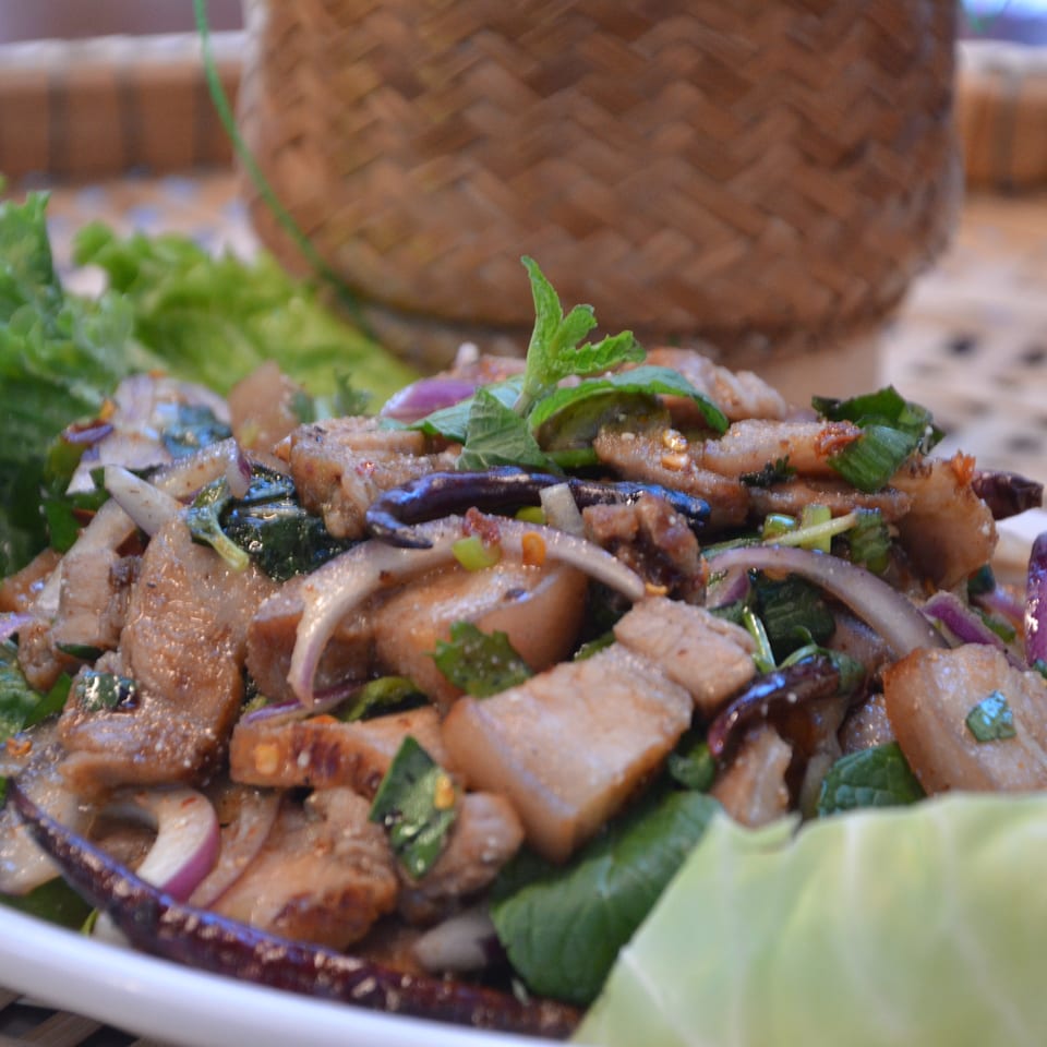Spicy grilled meat salad with red onion, herbs, chilies, and lettuce on a white platter.