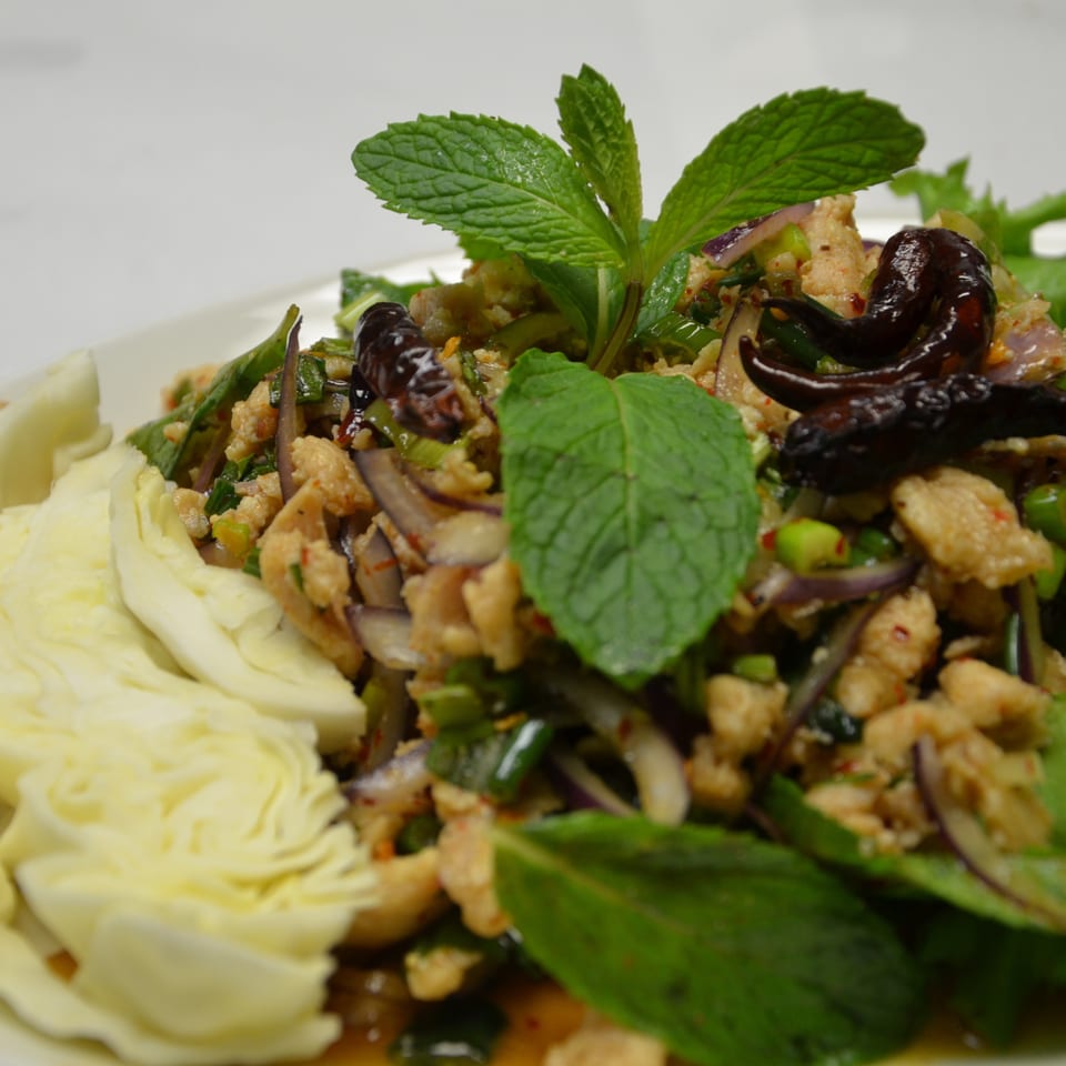Spicy minced meat salad with fresh mint, dried chilies, herbs, onions, cabbage, and lettuce on a plate.