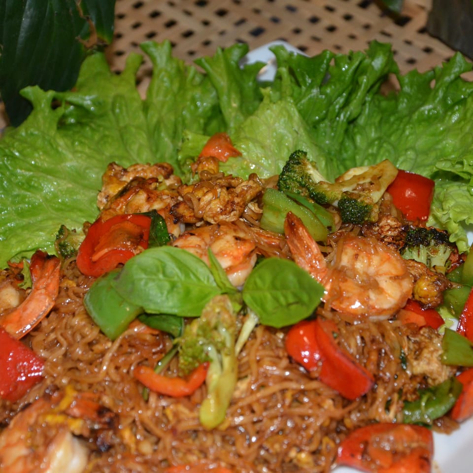 Plate of stir-fried noodles with shrimp, broccoli, bell peppers, lettuce, and fresh basil.