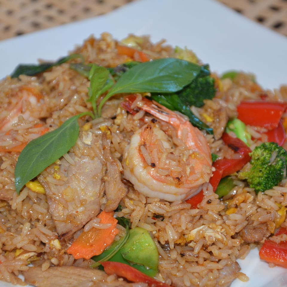 Plate of fried rice with shrimp, sliced meat, egg, broccoli, peppers, carrots, and fresh basil leaves.