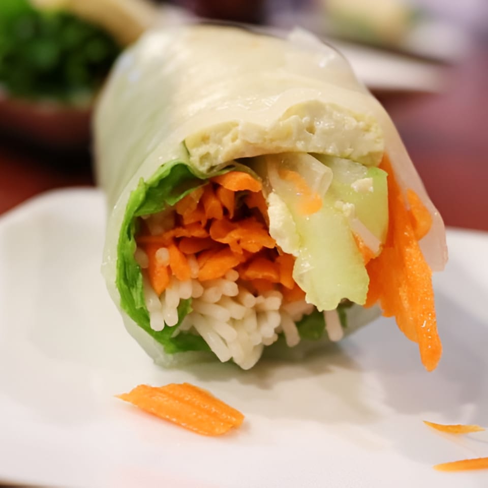 Close-up of a fresh Thai spring roll with rice, carrots, lettuce, and tofu on a white plate.