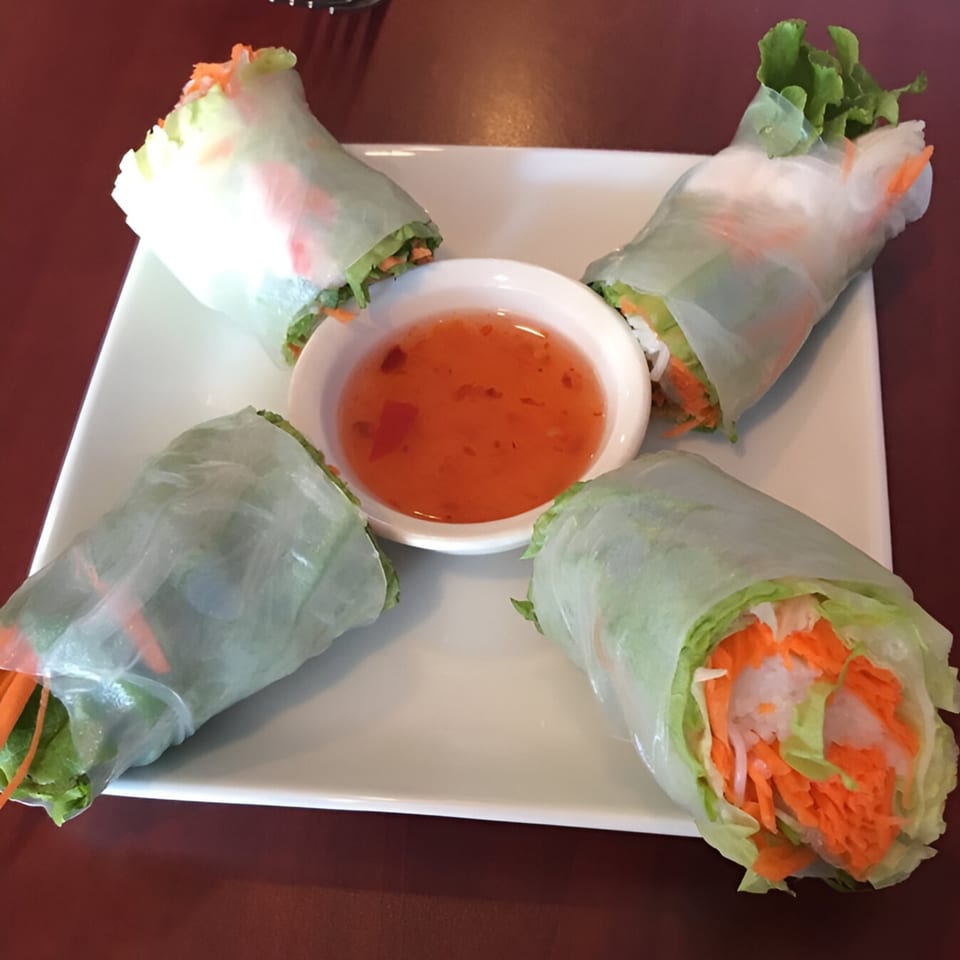 Four fresh Thai spring rolls with lettuce, carrots, and rice noodles, served with sweet chili sauce.